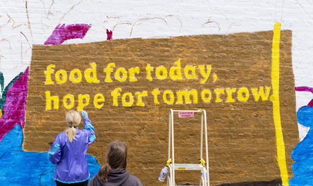 A volunteer paints the words of Lakeview Pantry's credo onto the wall.